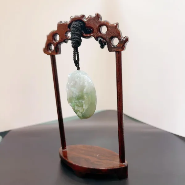 Carved jade pendant on wooden display stand.