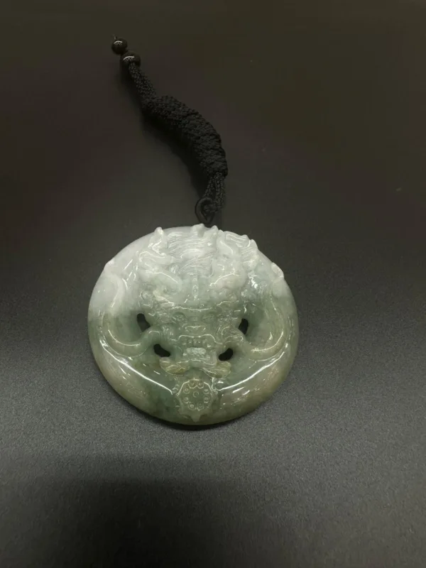 Jade dragon pendant with black cord on dark surface.