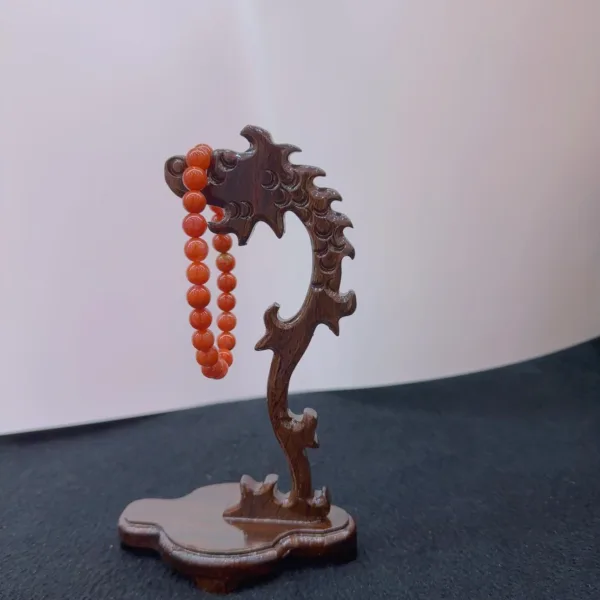 Carved wooden stand holding coral bead necklace.