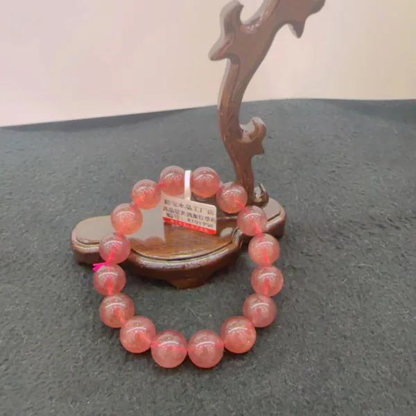 Pink bead bracelet on wooden stand against grey background.