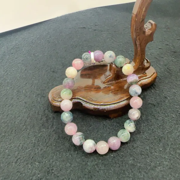 Beaded gemstone bracelet on wooden stand against dark surface.