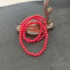 Red beaded necklace on black surface with wooden backdrop.