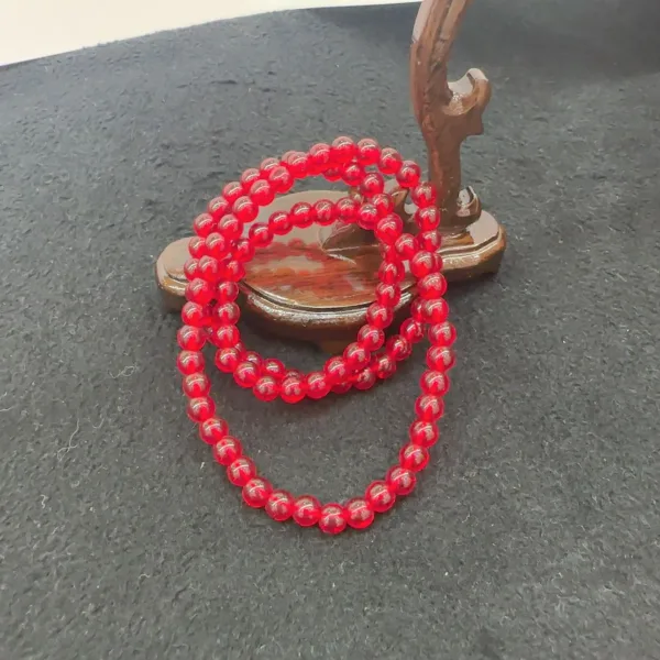 Red beaded necklace on black surface with wooden backdrop.