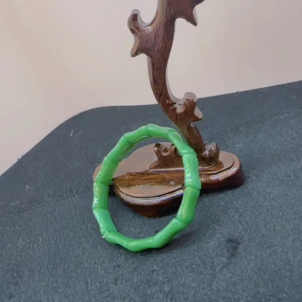 Green bracelet and wooden sculpture on black surface.