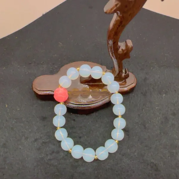 Opalite bead bracelet with pink accent on wooden stand.