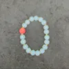 Opalite bracelet with single red bead on gray background.