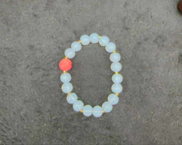 Opalite bracelet with single red bead on gray background.