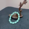 Mint green bracelet on dark background with wooden stand.