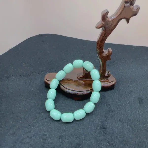 Mint green bracelet on dark background with wooden stand.