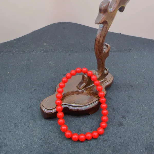 Red beaded bracelet on wooden sculpture stand.