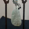 Carved jade pendant on wooden stand.