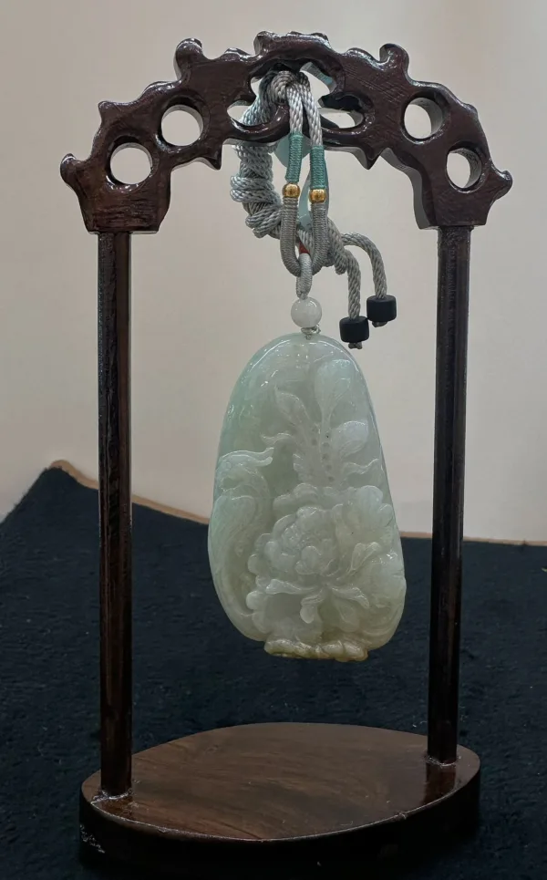 Carved jade pendant on wooden stand.