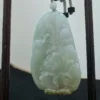 Carved jade pendant on wooden stand.