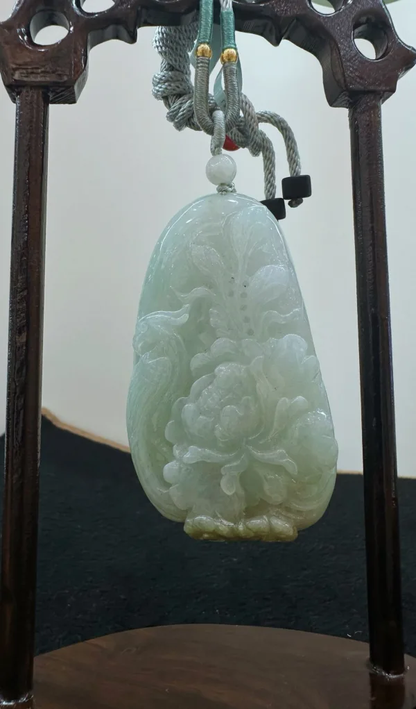 Carved jade pendant on wooden stand.