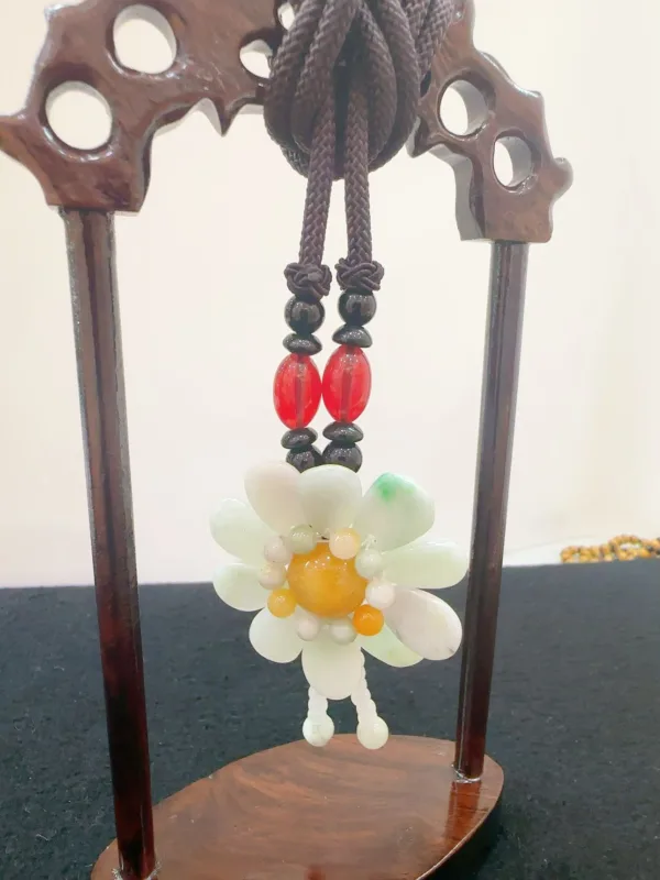 Jade flower pendant on wooden stand.