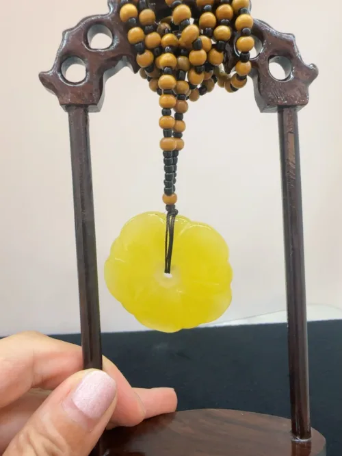 Beaded necklace with yellow jade pendant on wooden stand.