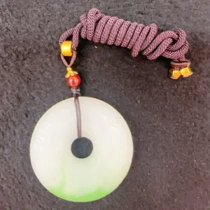 Jade pendant with braided cord on dark background.