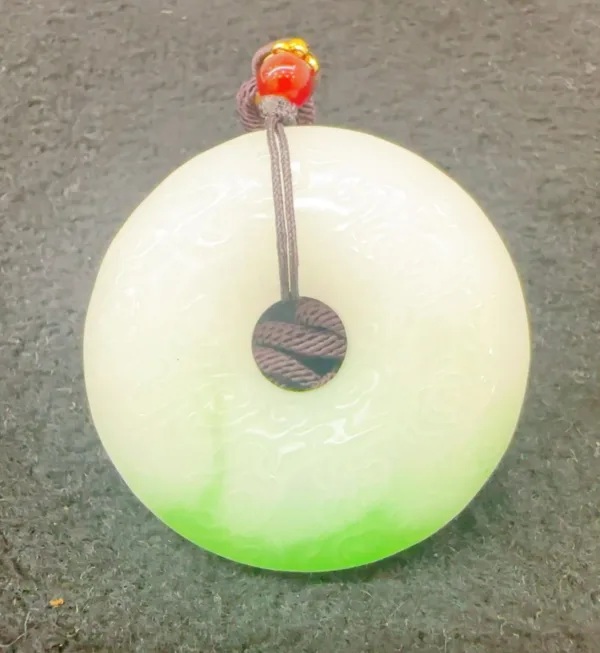 Jade pendant with red bead on top.