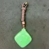 Green jade pendant with brown cord on dark surface.