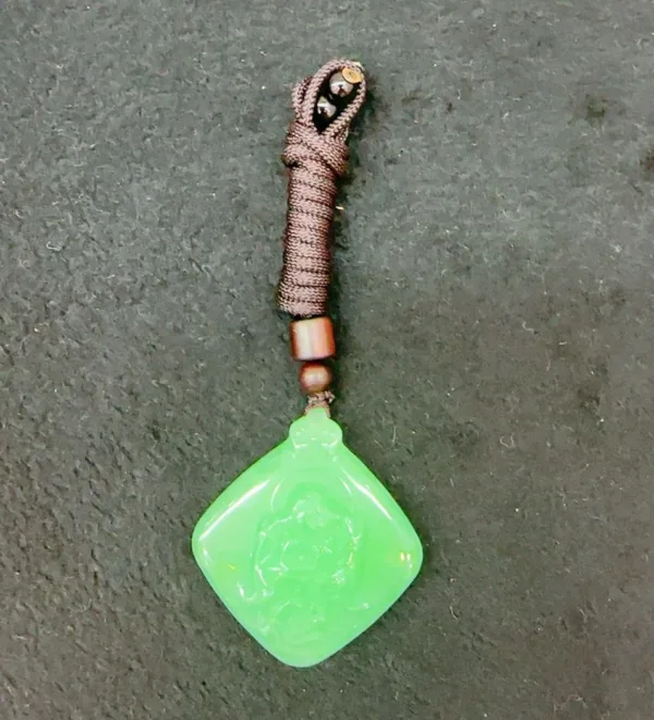 Green jade pendant with brown cord on dark surface.