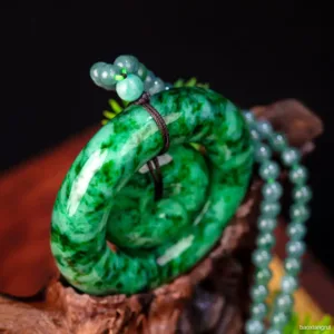 Carved jade bracelet with beads on wooden surface.