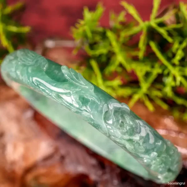 Carved jade bangle close-up with greenery background.