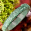 Carved jade bangle close-up with blurred green background.