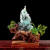 Carved jade figurine with wooden base and greenery.