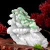 Intricate jade carving on wooden base with red foliage.