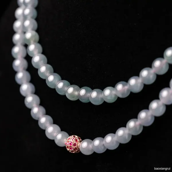 Elegant pearl necklace with ruby clasp on black background.