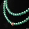 Green jade necklace with gold clasp on black background.