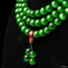 Green bead necklace with red pendant on black background.