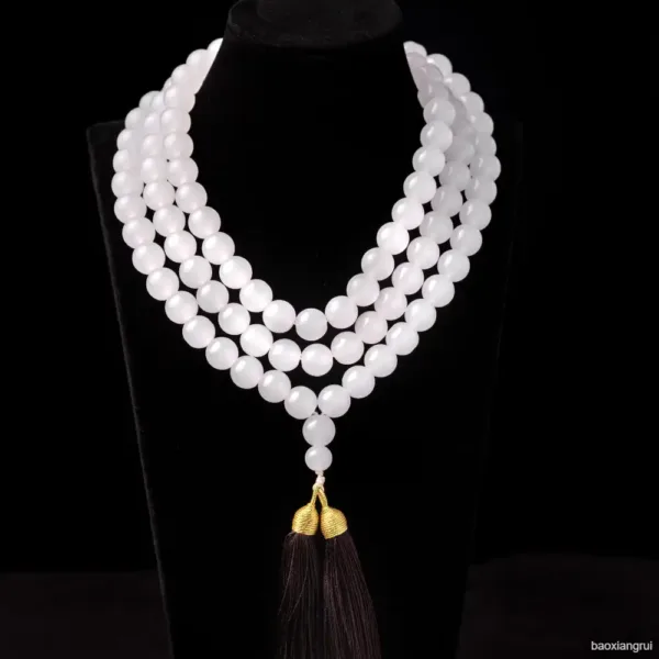 White beaded necklace with tassel on black display.