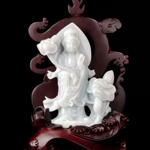 Carved jade Guanyin statue with wooden backdrop.